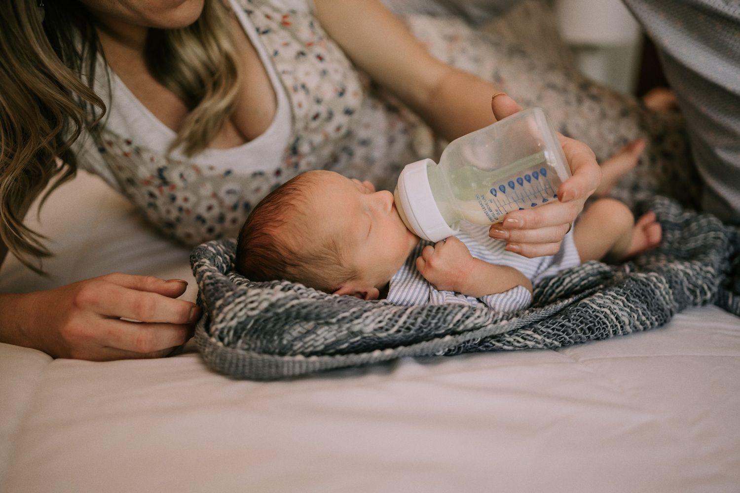A newborn baby on a gray blanket being bottle-fed while resting peacefully.