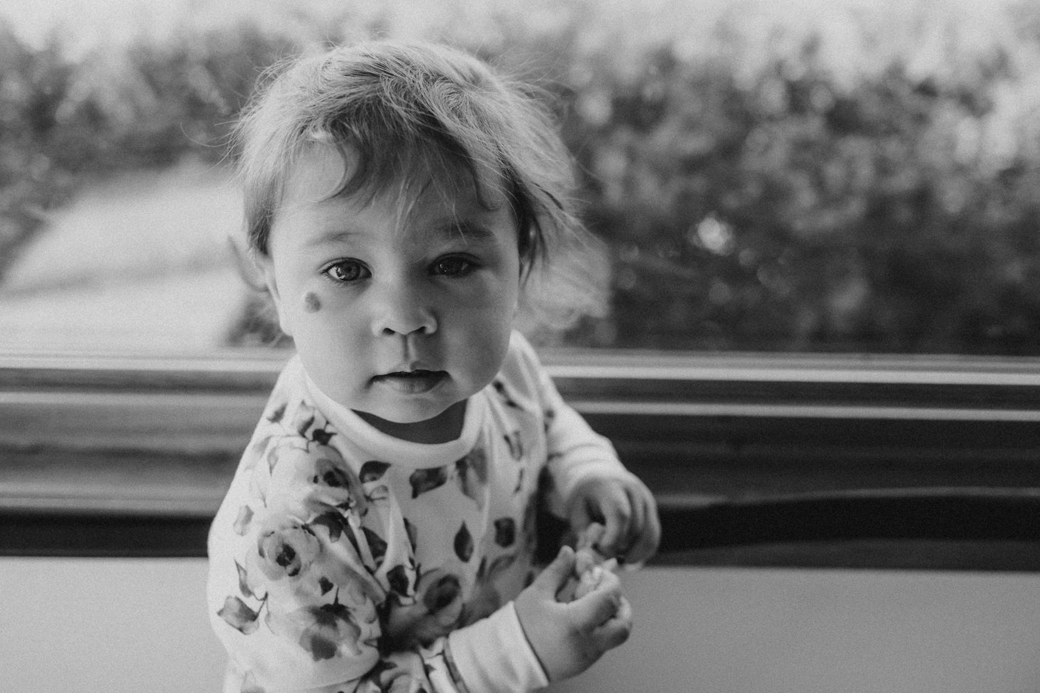 Close-up black and white portrait of a toddler in floral clothing looking at camera.