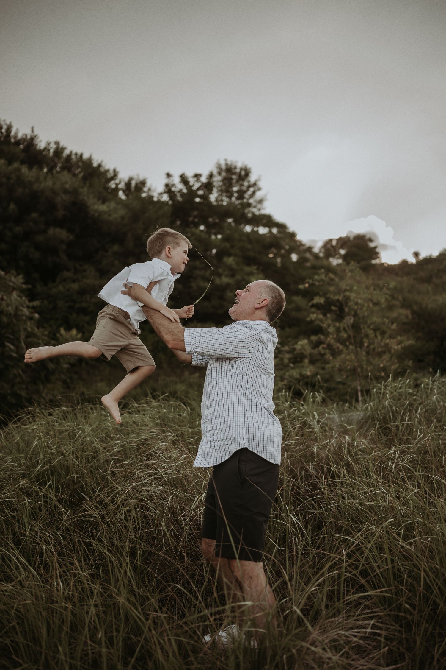 A playful moment captured as a person lifts a child high into the air on a grassy hillside.