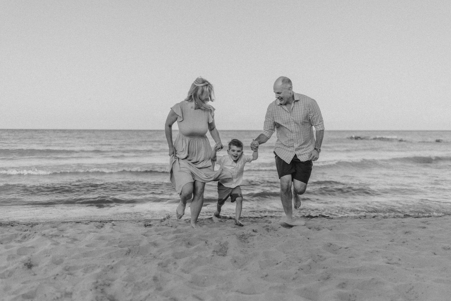 Black and white image of a family holding hands while walking along the shoreline.