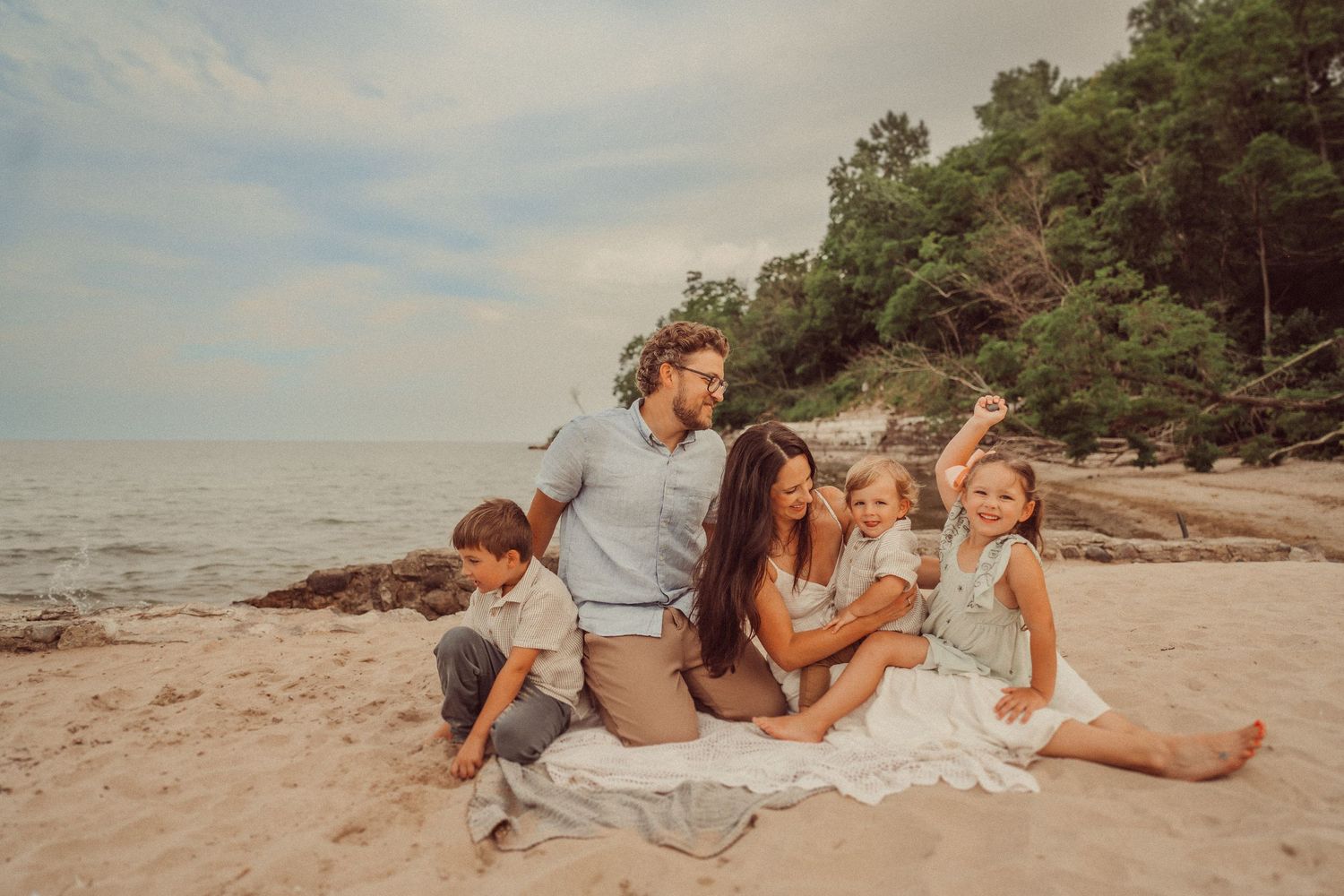 A casual beach gathering with people sitting on a blanket during golden hour.