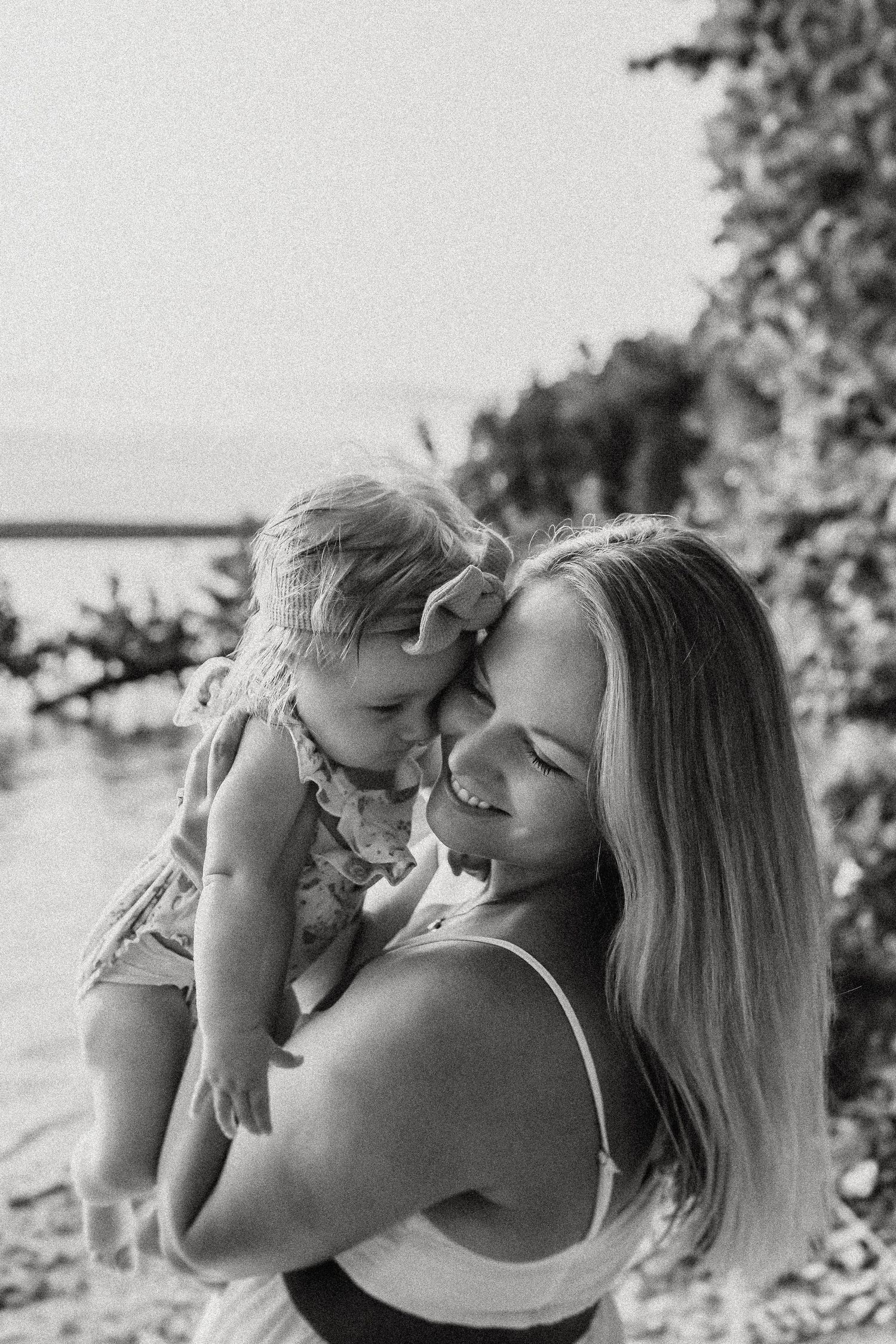 Black and white portrait of tender moment between parent and child by water.