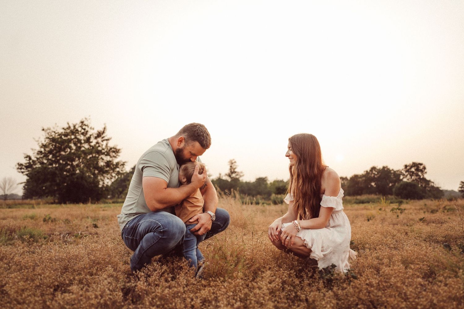 Family sitting together on dry grass in a field during golden hour.