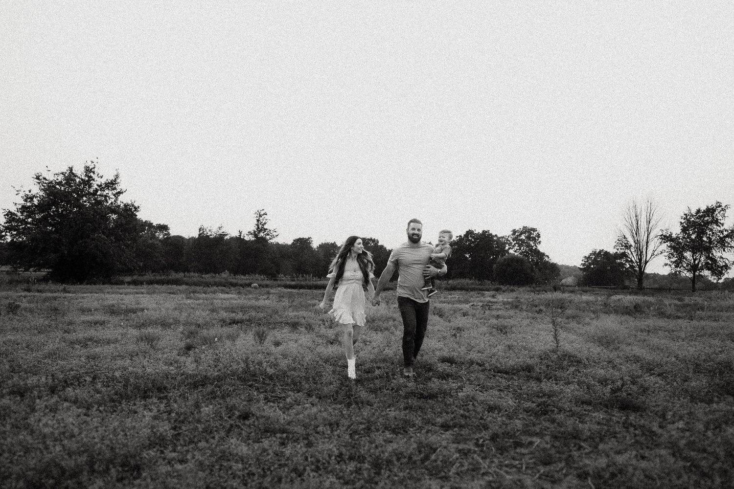 Black and white photo of a couple walking hand in hand through an open field.