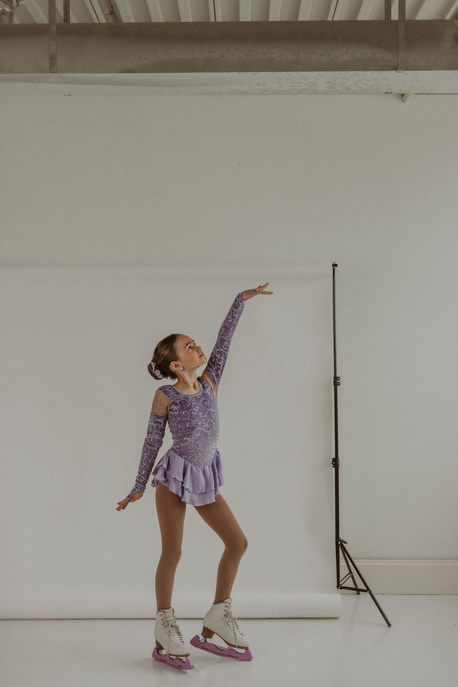 Figure skater in purple dress strikes graceful pose on ice skates in studio setting.