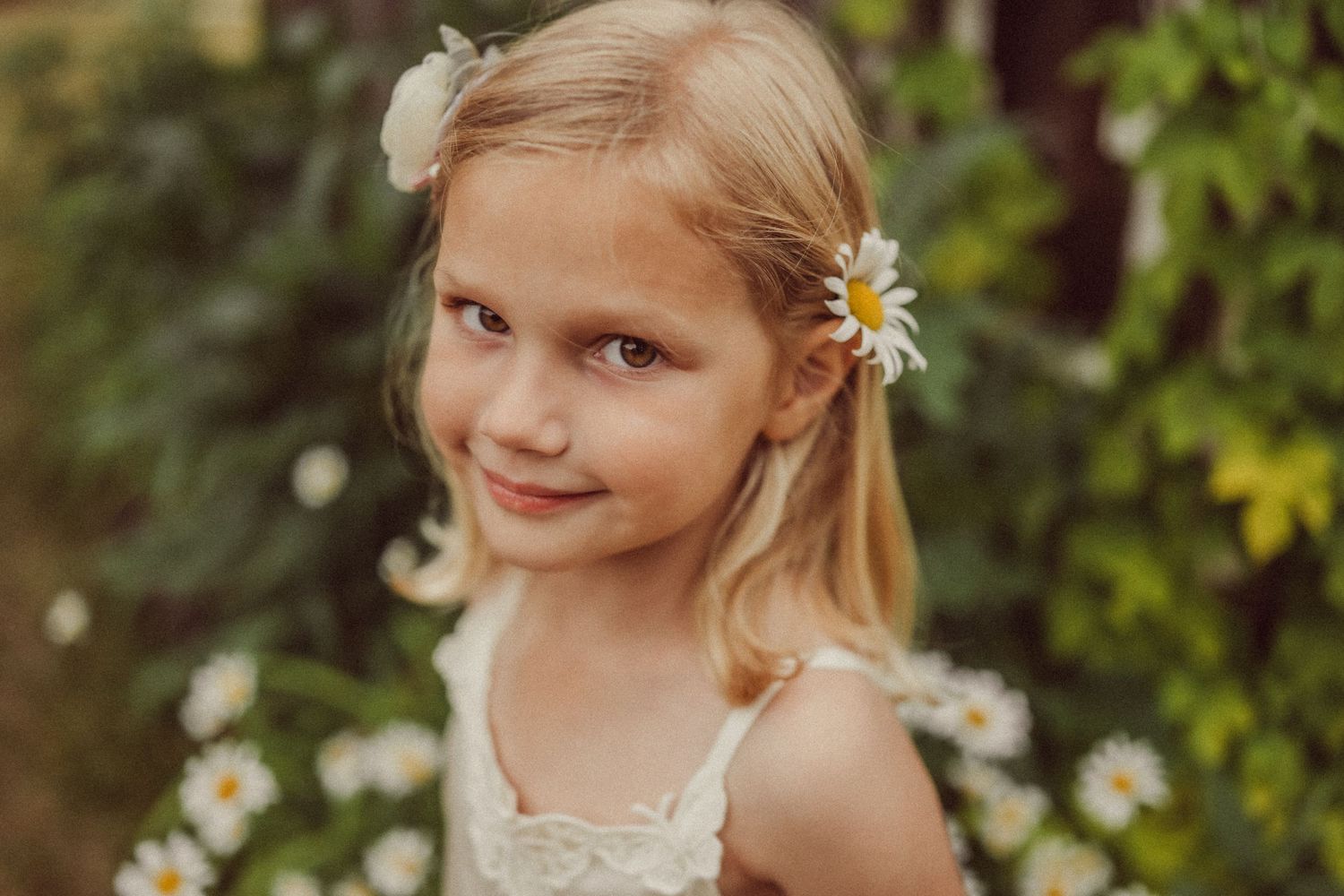 Portrait of a child wearing a white summer dress with daisies in their hair.