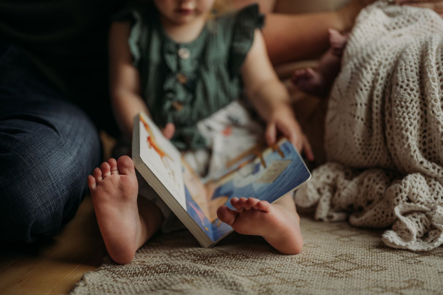 Little feet peek out while reading a book on a cozy blanket.