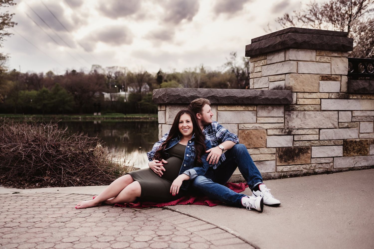 Couple relaxing on stone wall during outdoor maternity photoshoot.