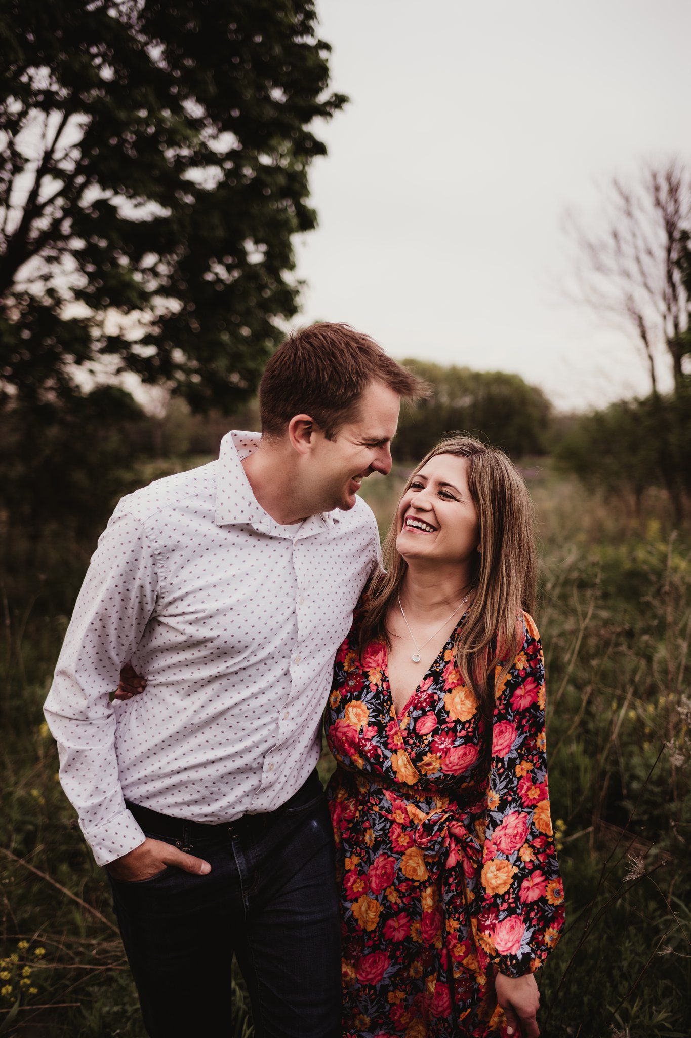 A candid moment of laughter shared between a couple in a field at sunset.