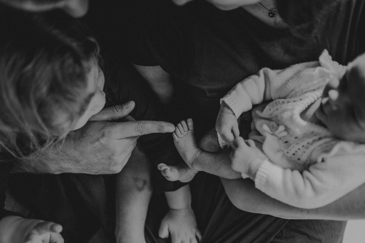 Black and white close-up of hands gently touching a baby in white clothing.