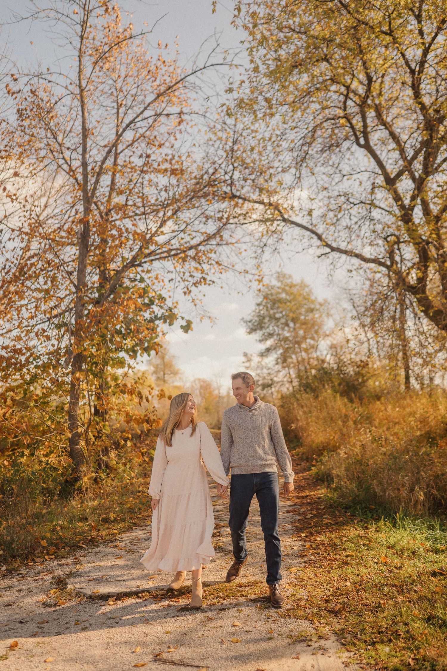 A couple walks hand in hand through a scenic fall landscape with golden leaves.
