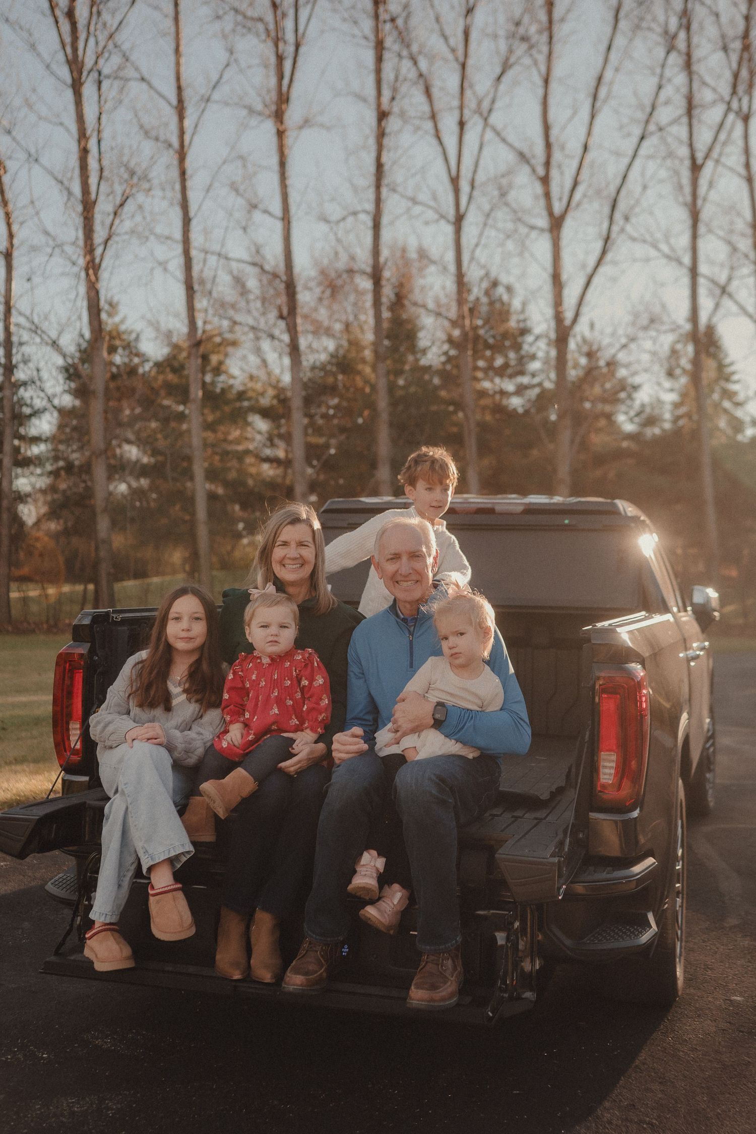 Family sitting together in the back of a pickup truck at sunset with trees in background.