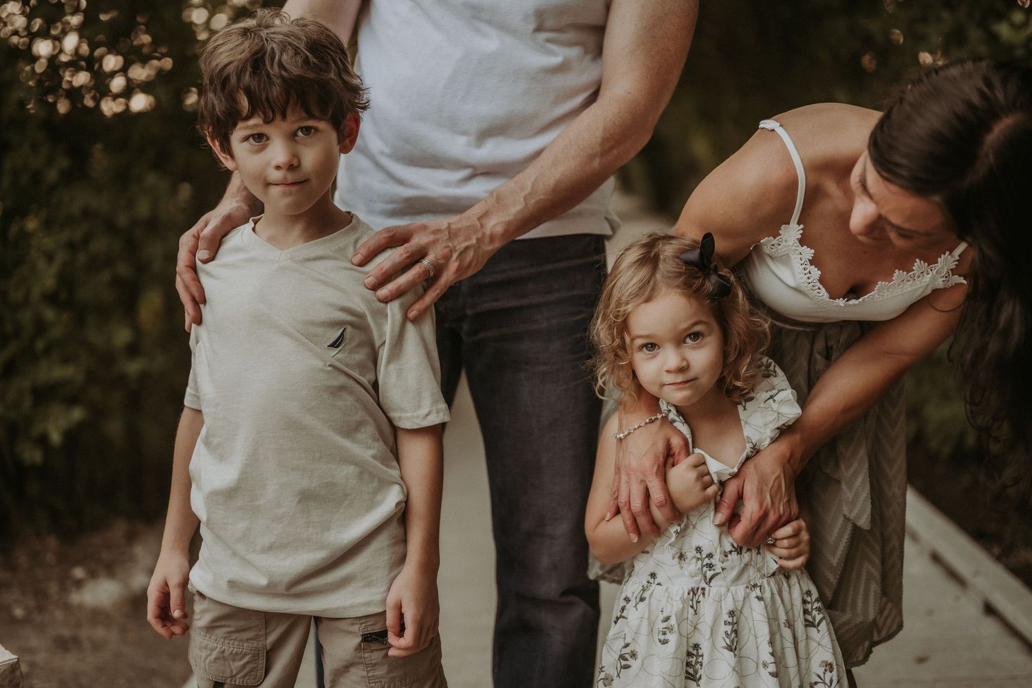 A candid family portrait captures tender moments between parents and children outdoors.