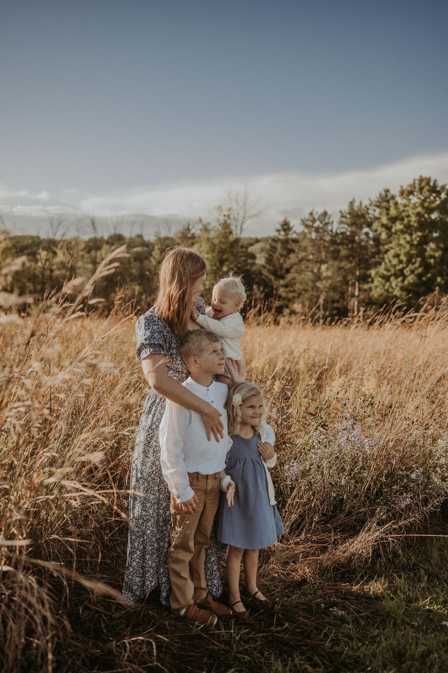 Family standing together in tall golden grass with mountains and pine trees in background.