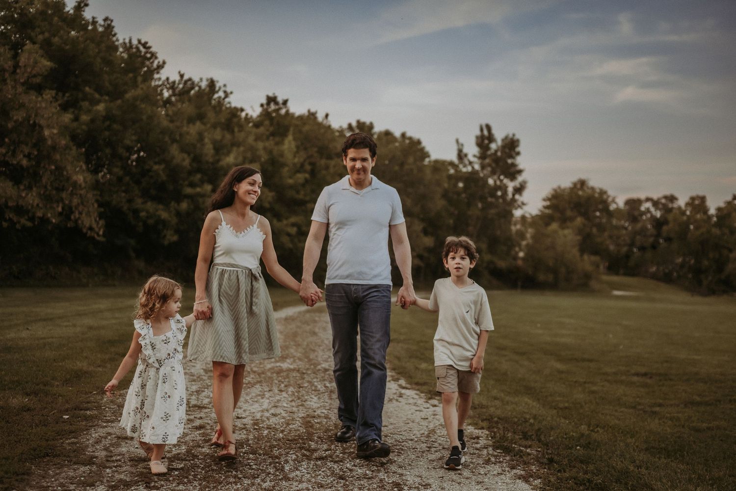 A family of four strolls hand-in-hand down a country path at sunset.