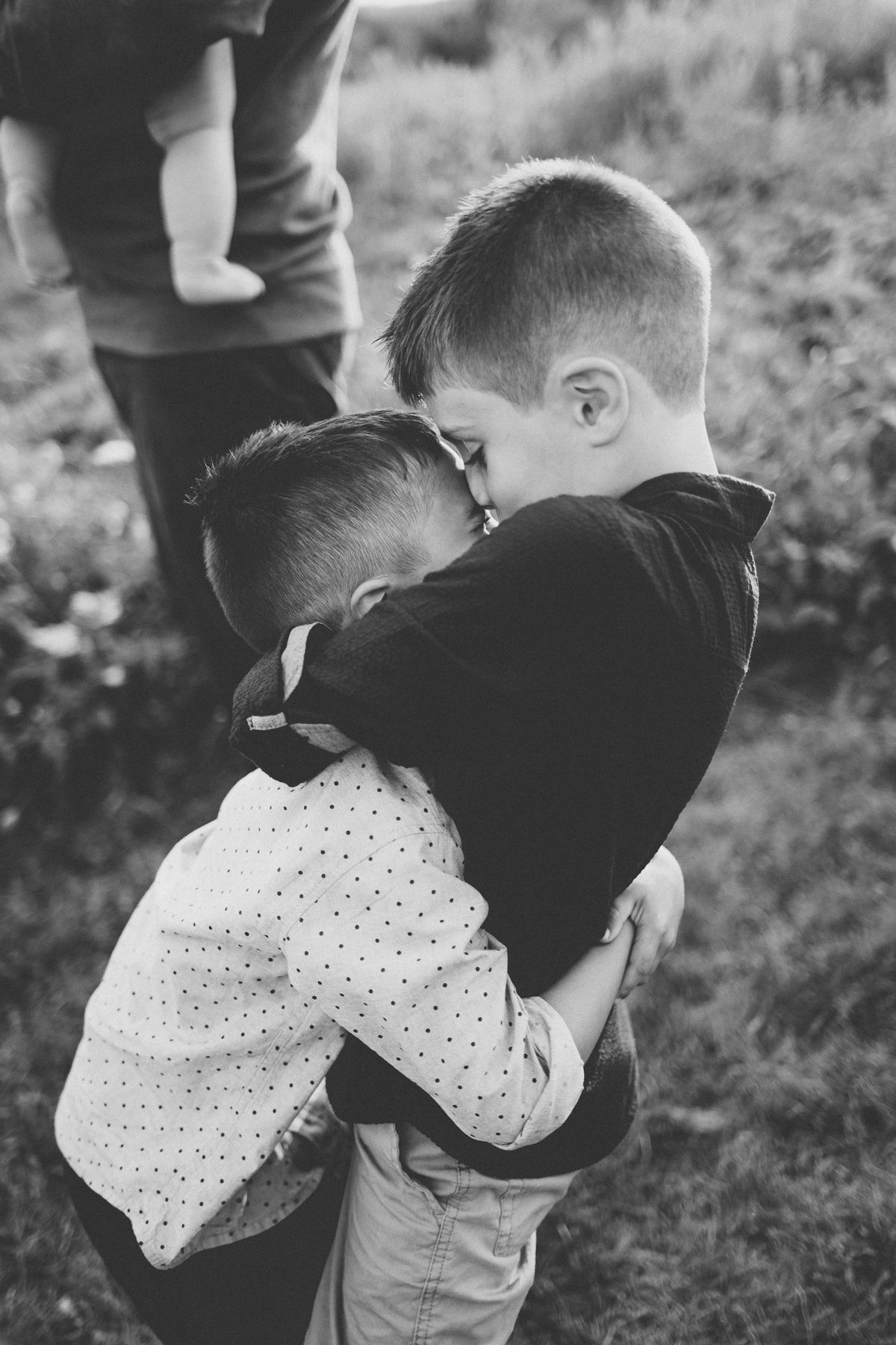 Black and white photo of two children hugging in a field with tender emotion.