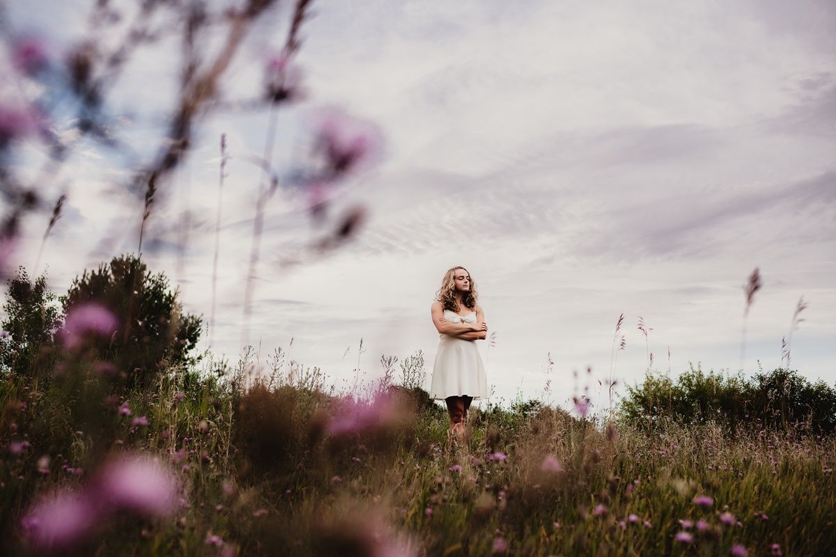 Dreamy distant figure in white dress standing among wildflowers at sunset.