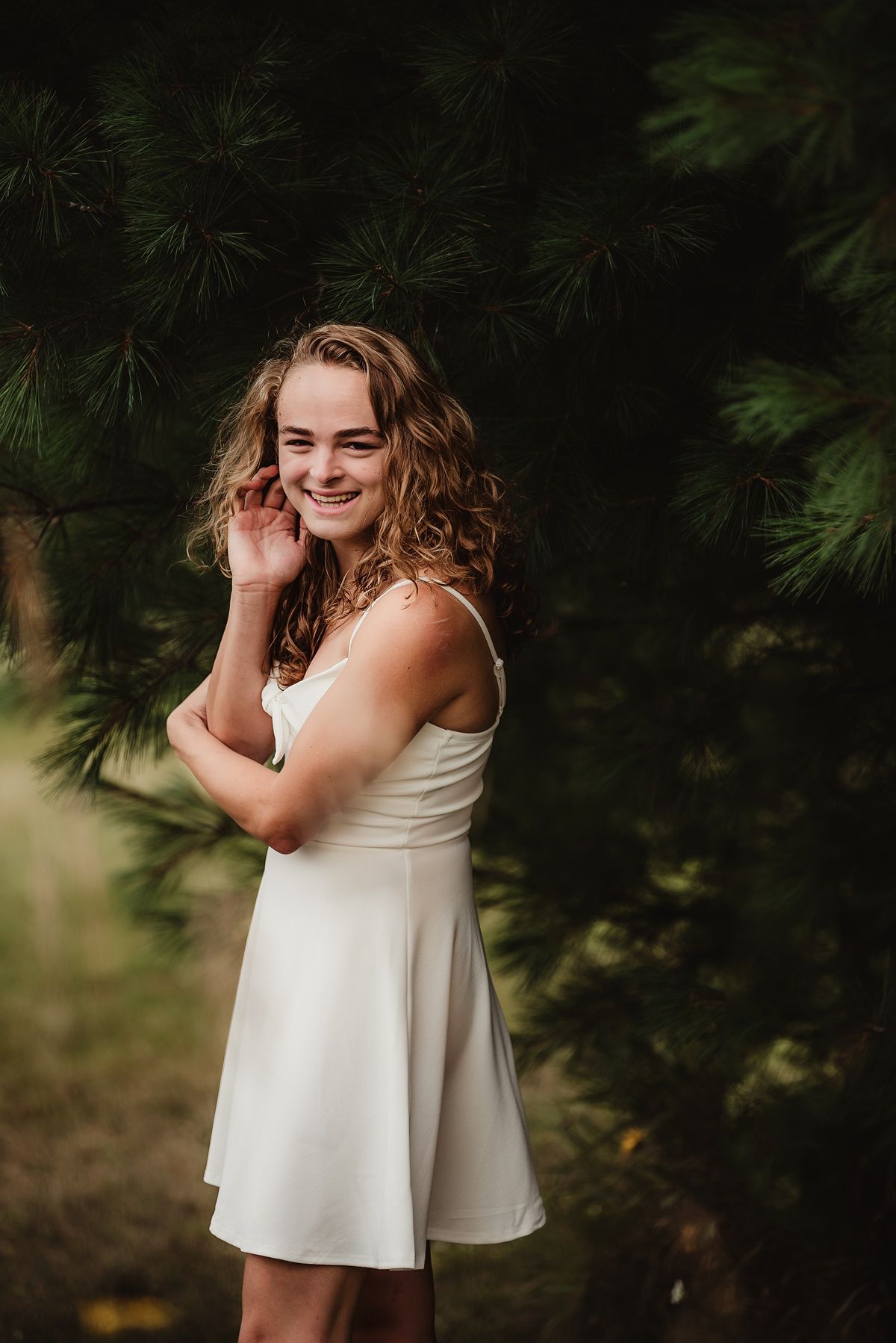 Portrait against pine trees in white summer dress with natural lighting.
