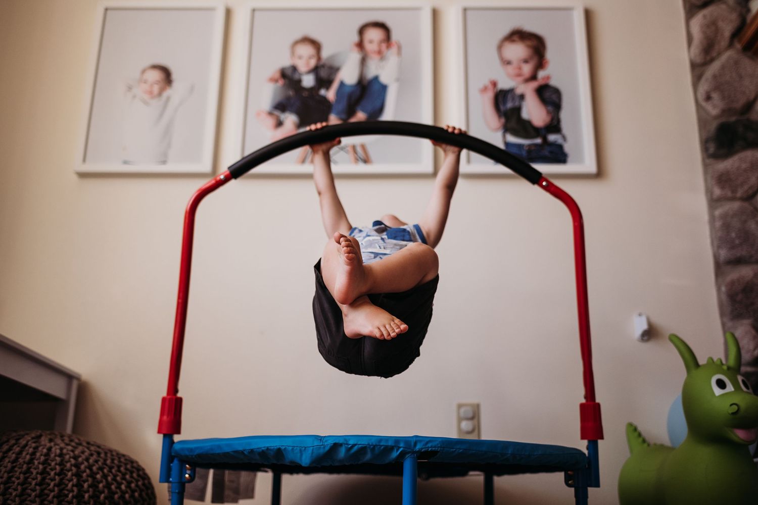 A child performs a flip on a small indoor gymnastics bar with framed photos on the wall.