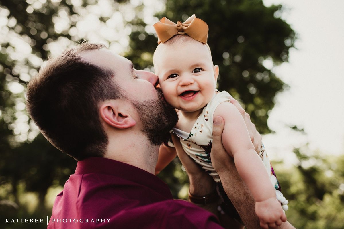 A joyful outdoor portrait showing tender interaction between adult and laughing baby with bow.