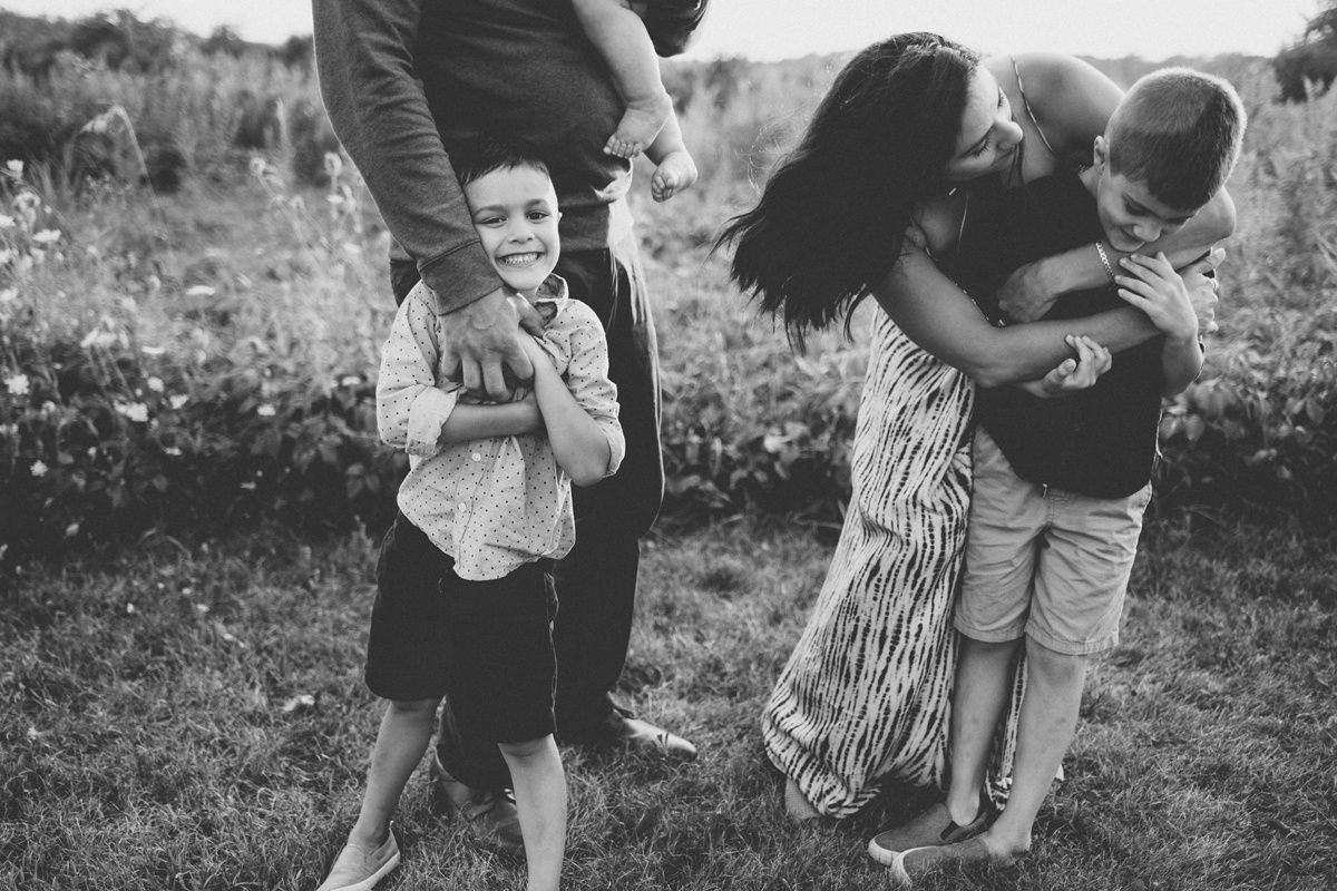 Black and white candid photo of family playing and laughing together in a wildflower field.