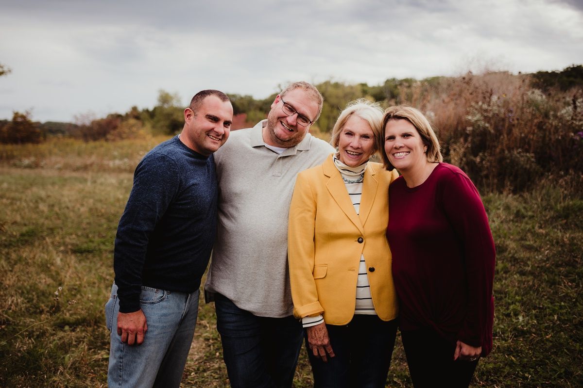 Four people stand close together smiling outdoors on an overcast day.