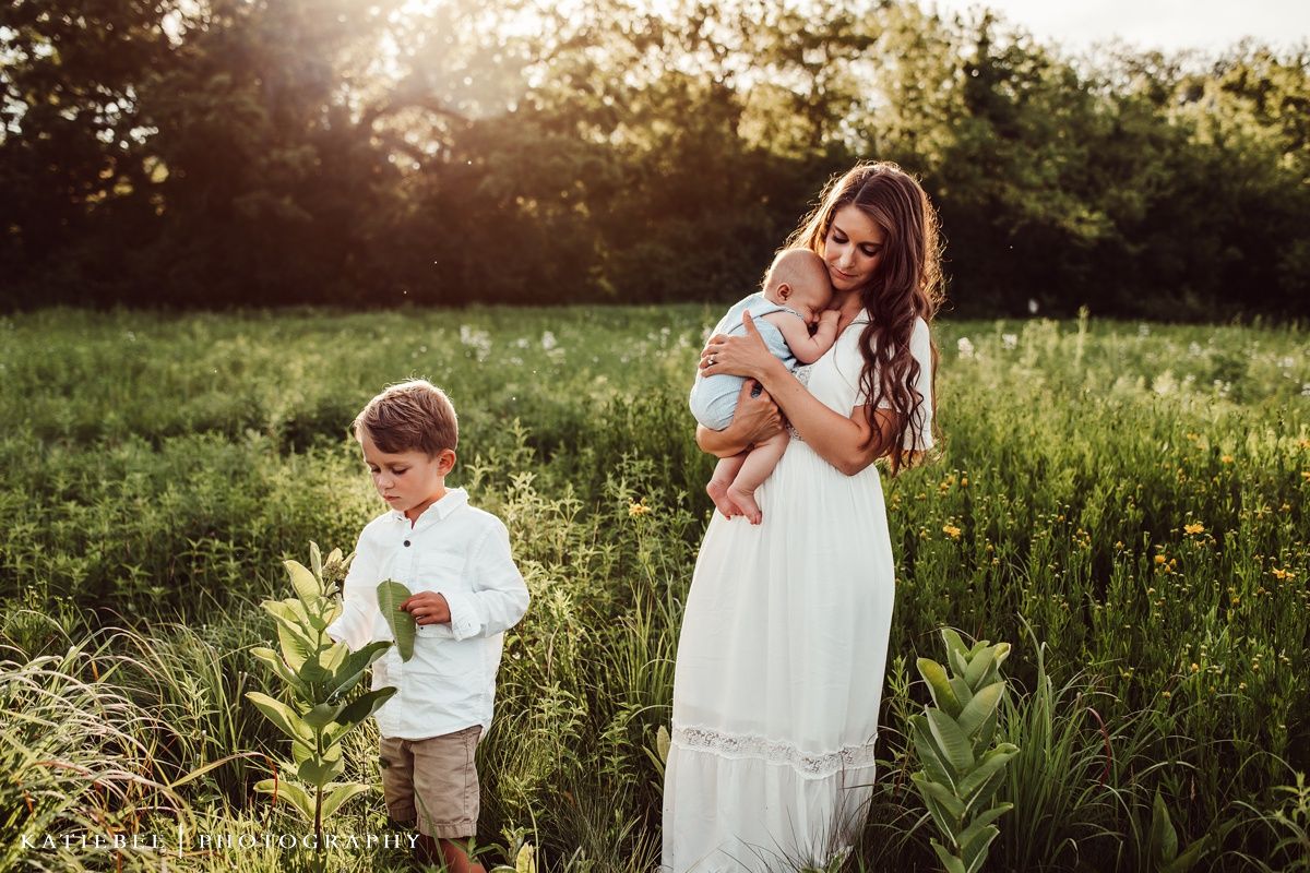Mother in white dress with children in sunlit meadow during golden hour.