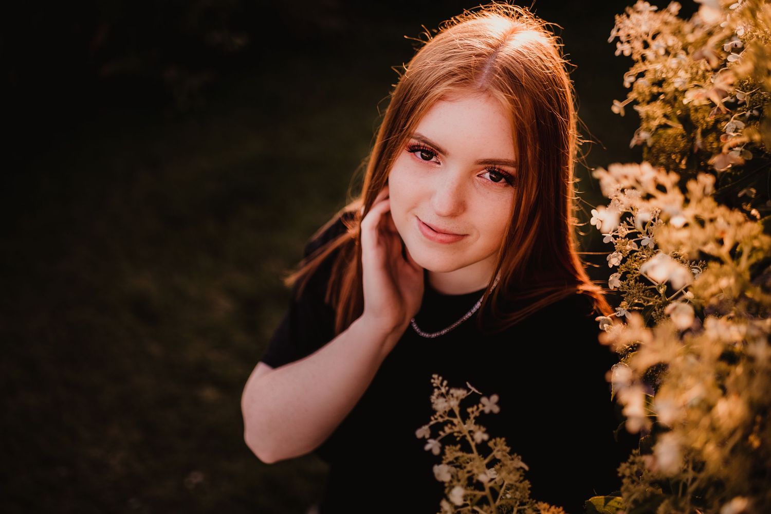 Portrait of a person in black sweater against autumn foliage at sunset.