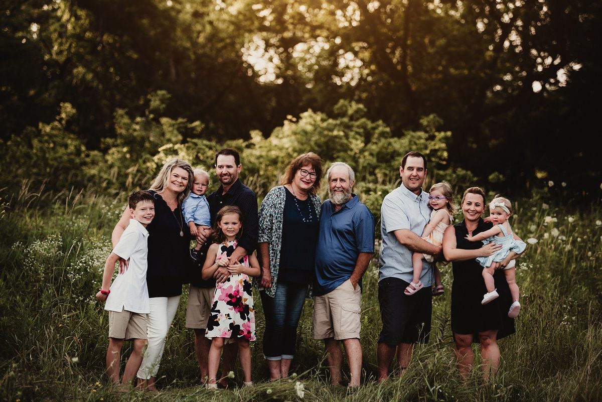 A large family group poses together at sunset in a wildflower meadow with an old barn in the background.