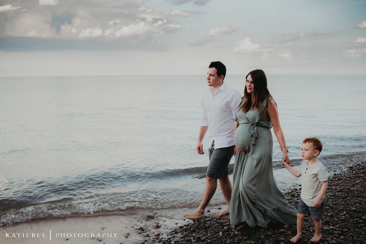 A family walks along a peaceful beach shore at dusk with calm waters in the background.