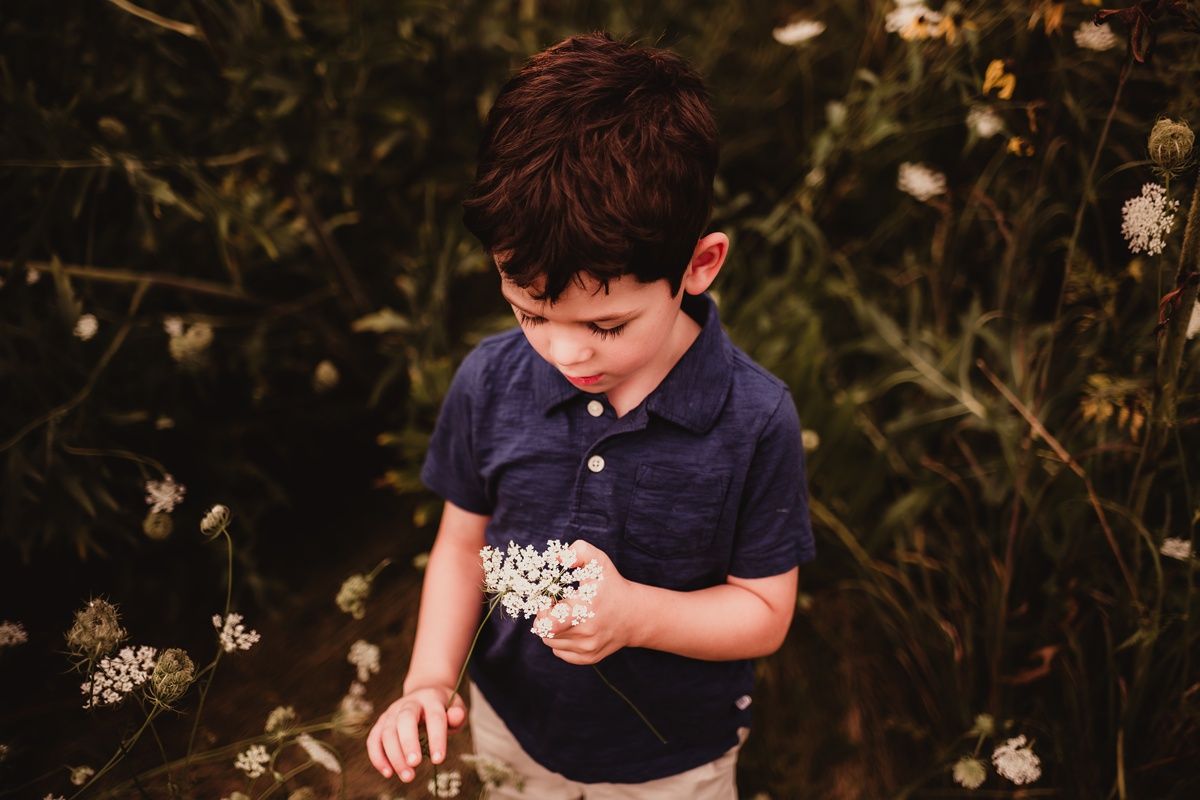 Young child in navy polo examines flowers in garden setting.