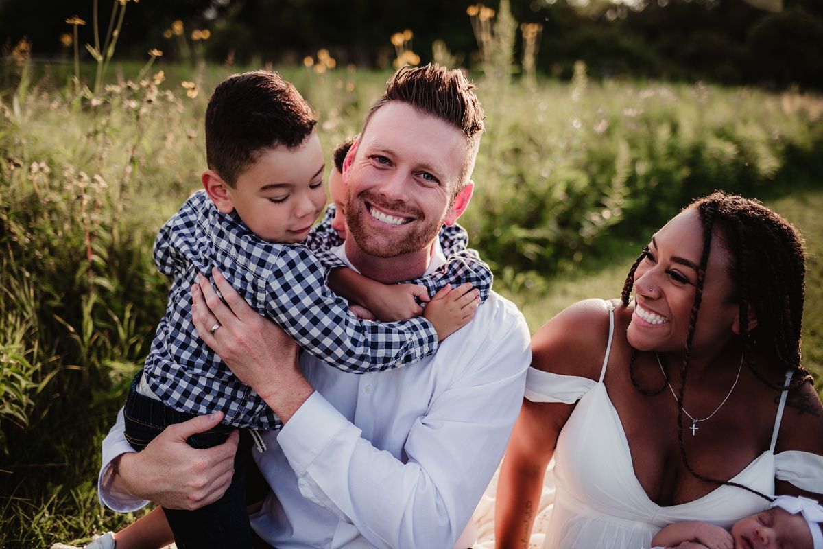 A joyful family moment captured in a sunlit meadow showing affectionate embrace and laughter.