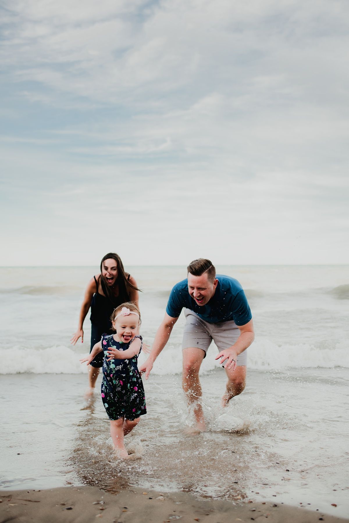 A family splashes and plays together in the shallow ocean waves on a sunny beach.