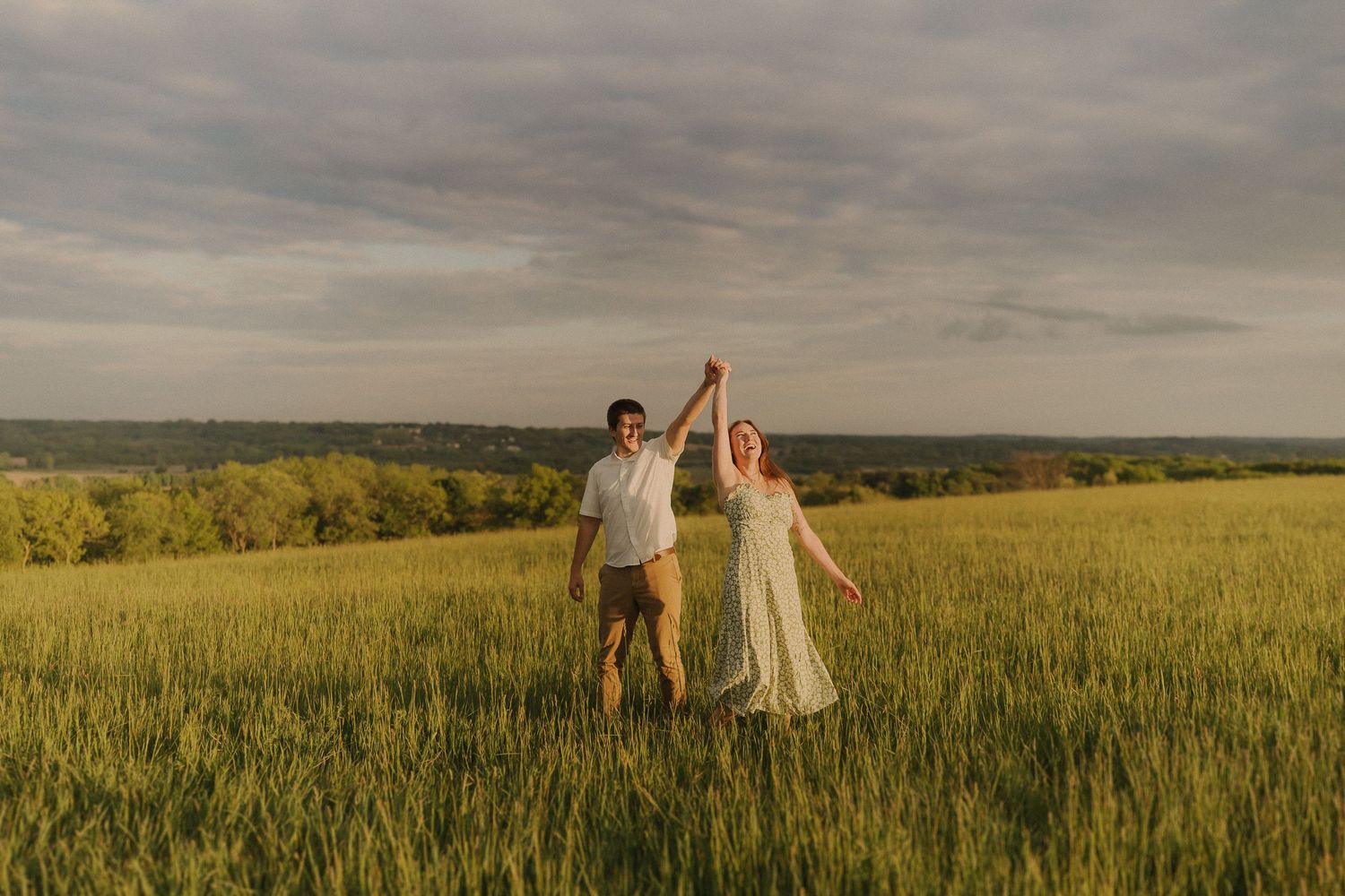 A couple celebrates with raised arms in a golden sunset field.