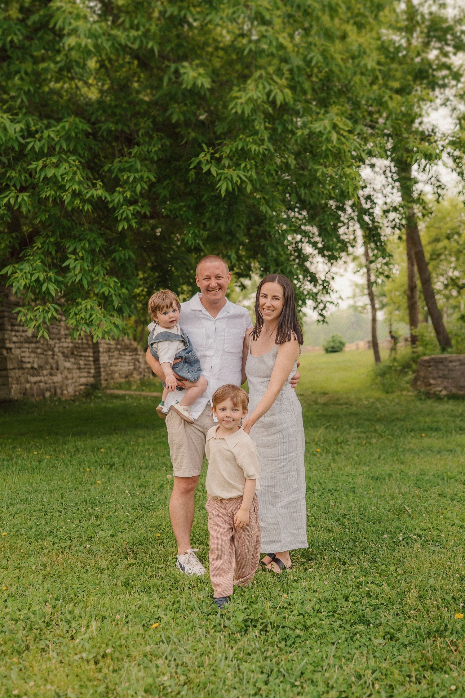 A family in coordinated outfits poses together for a portrait in front of lush greenery.