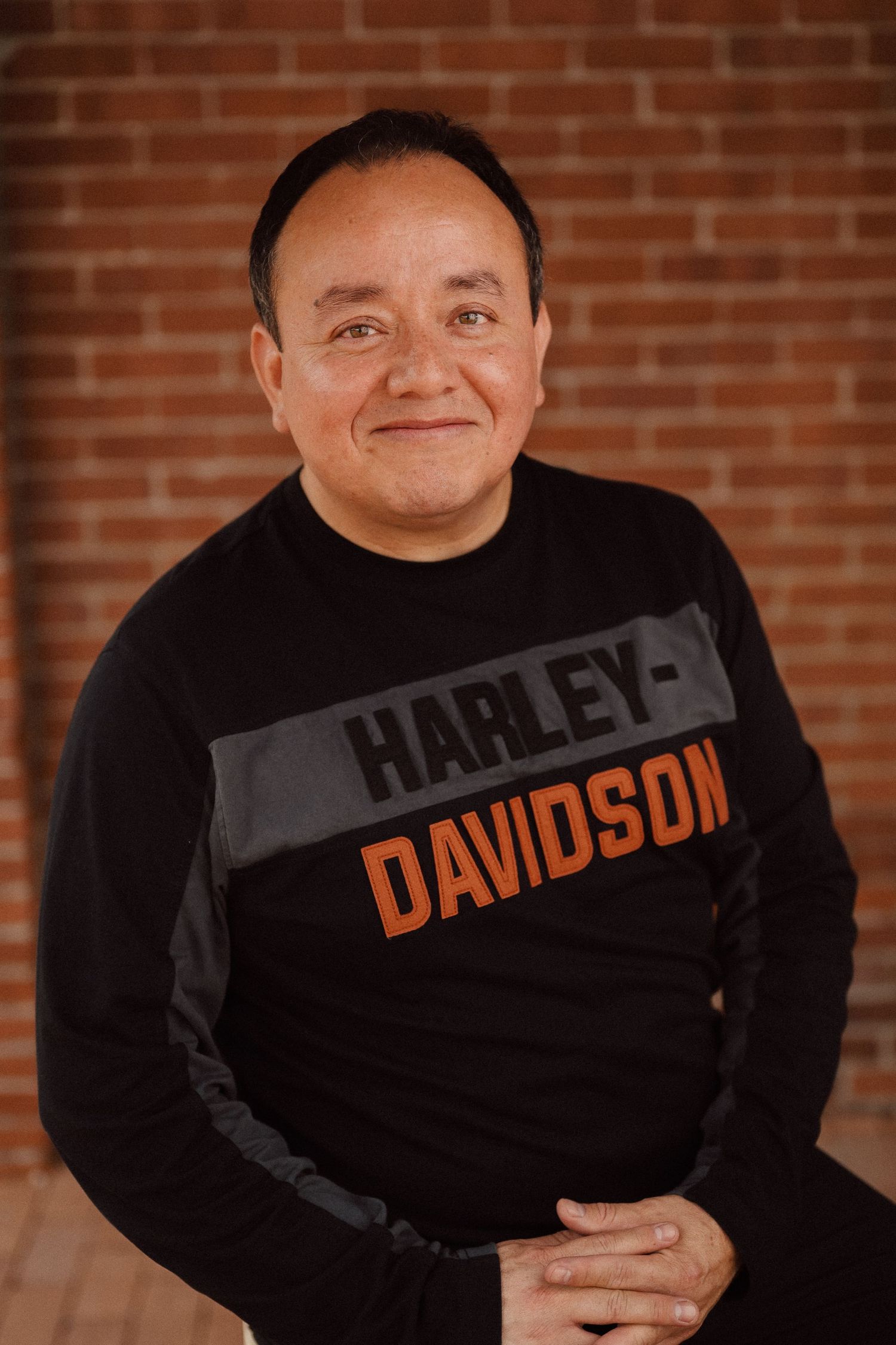 Person in a Harley-Davidson branded black t-shirt posing against a rustic brick backdrop.