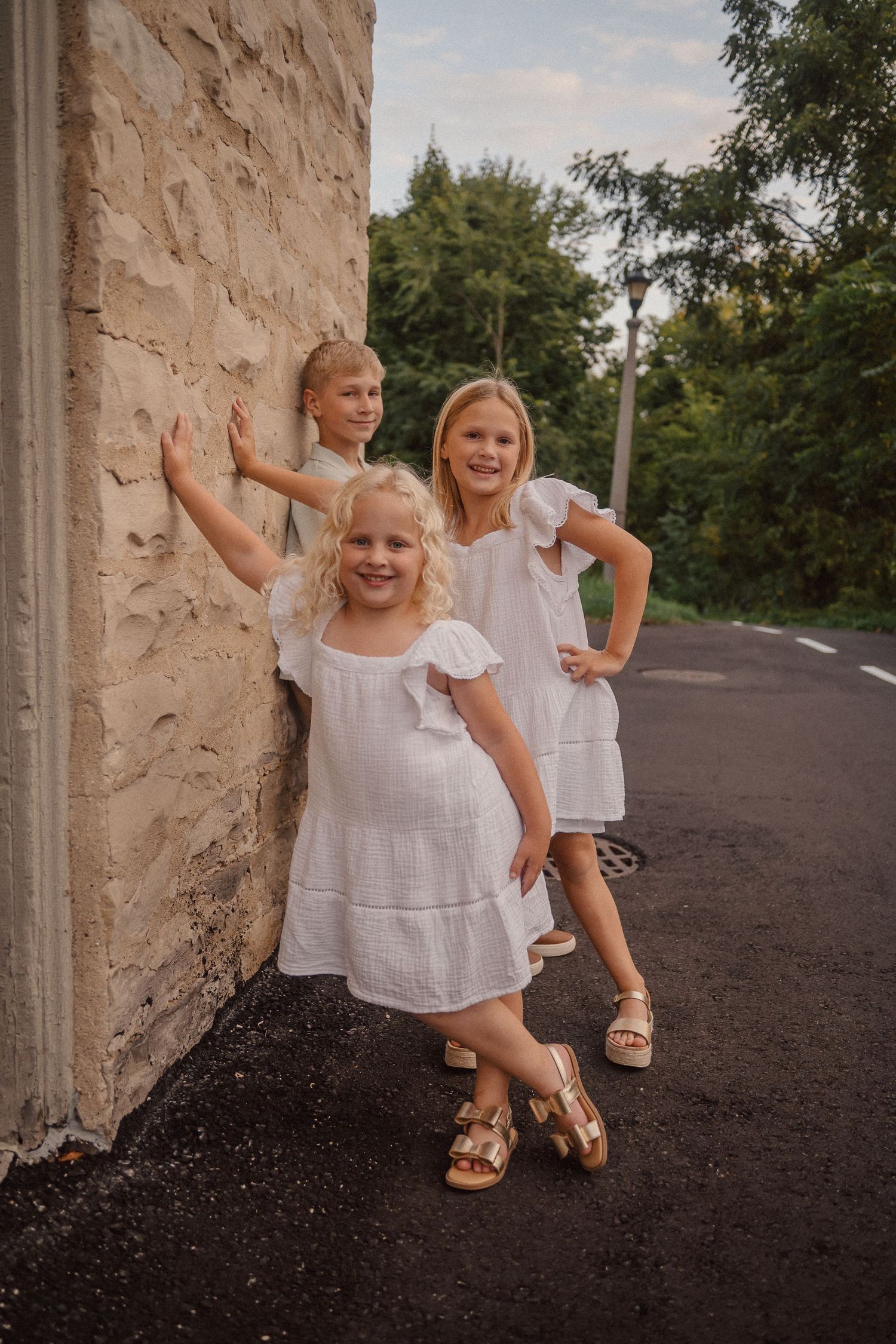 Playful poses against a textured stone wall on a paved path during an outdoor photo session.