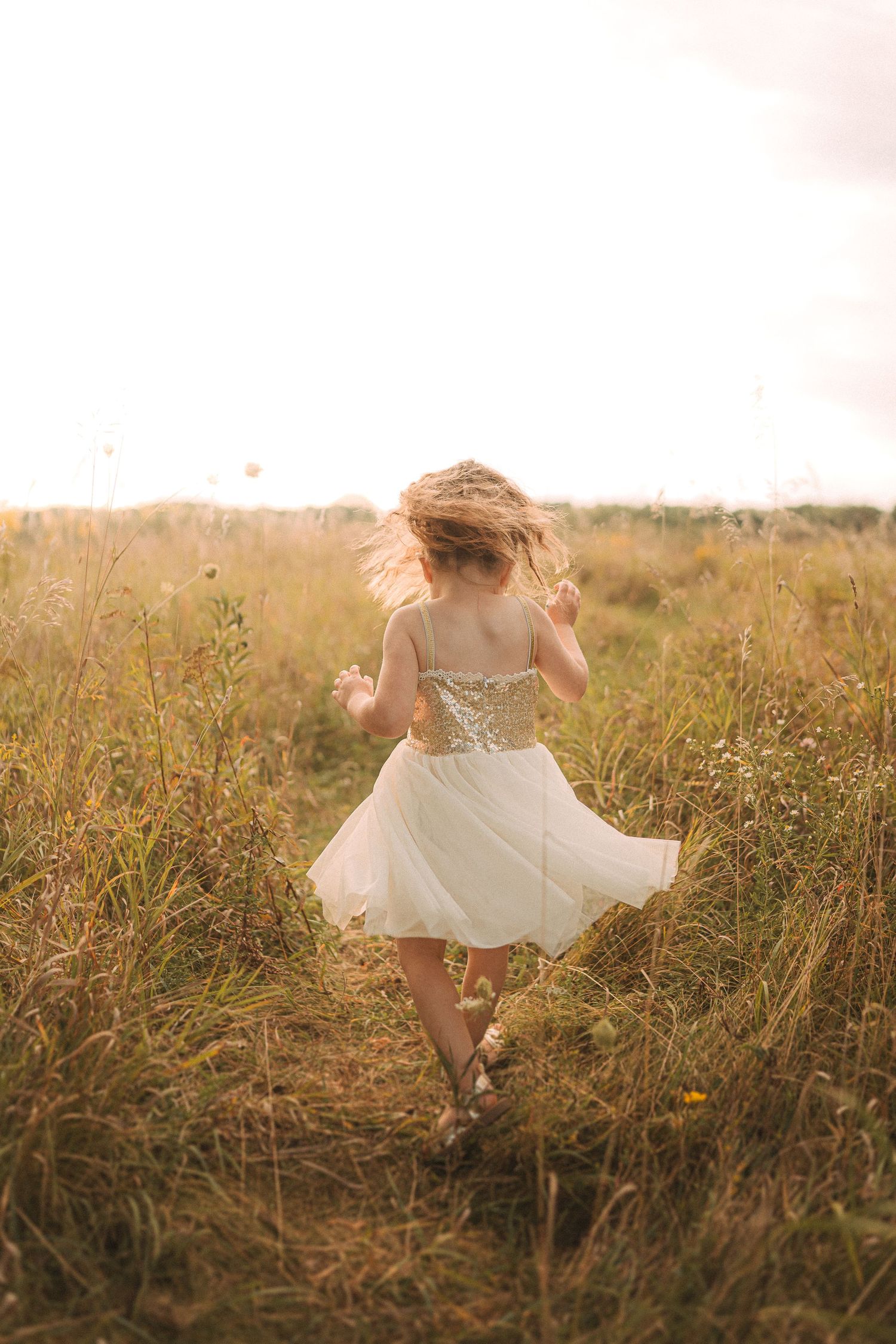 Girl in white dress twirling through golden field at sunset.