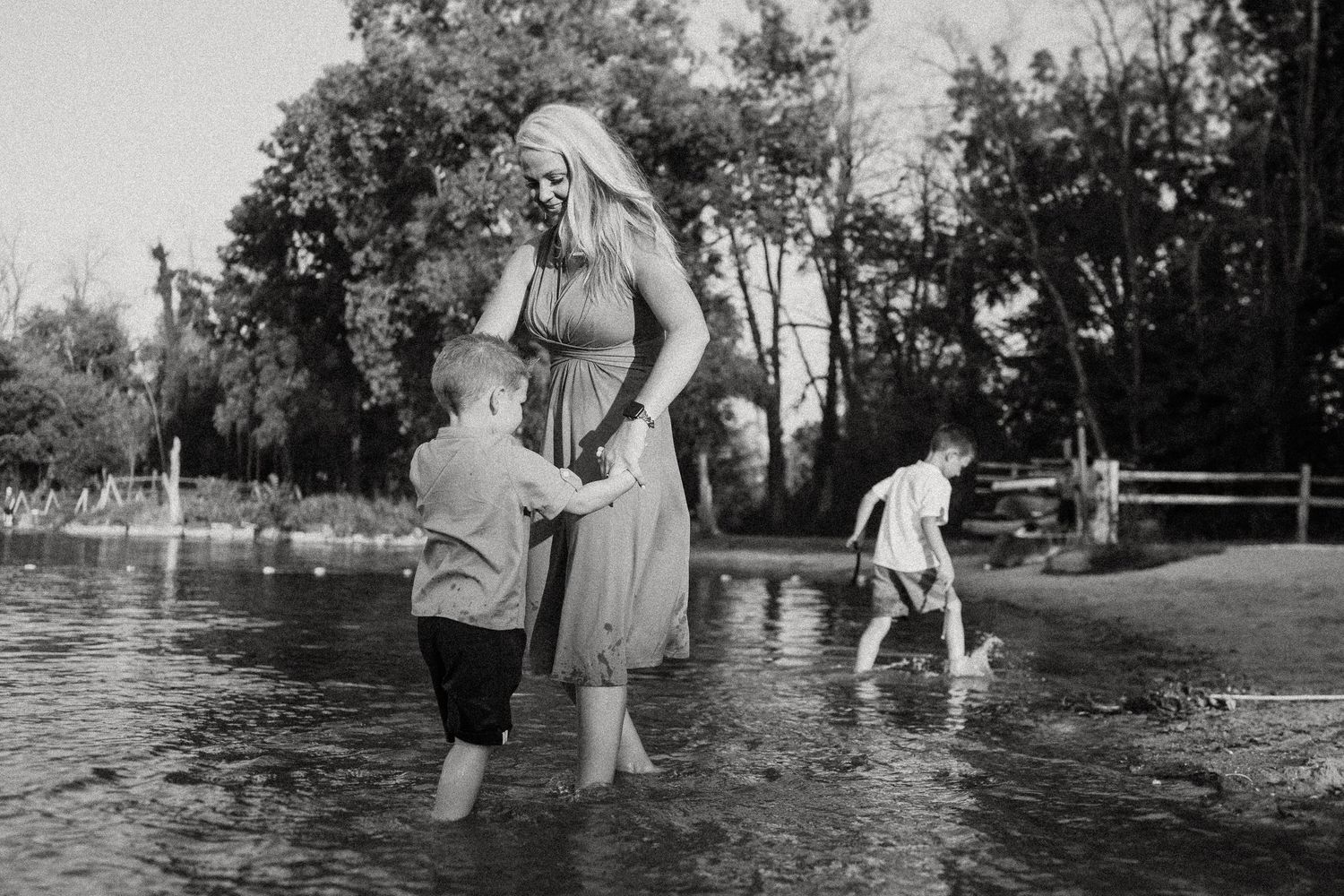 A black and white photo of people wading in shallow water near trees on a summer day.