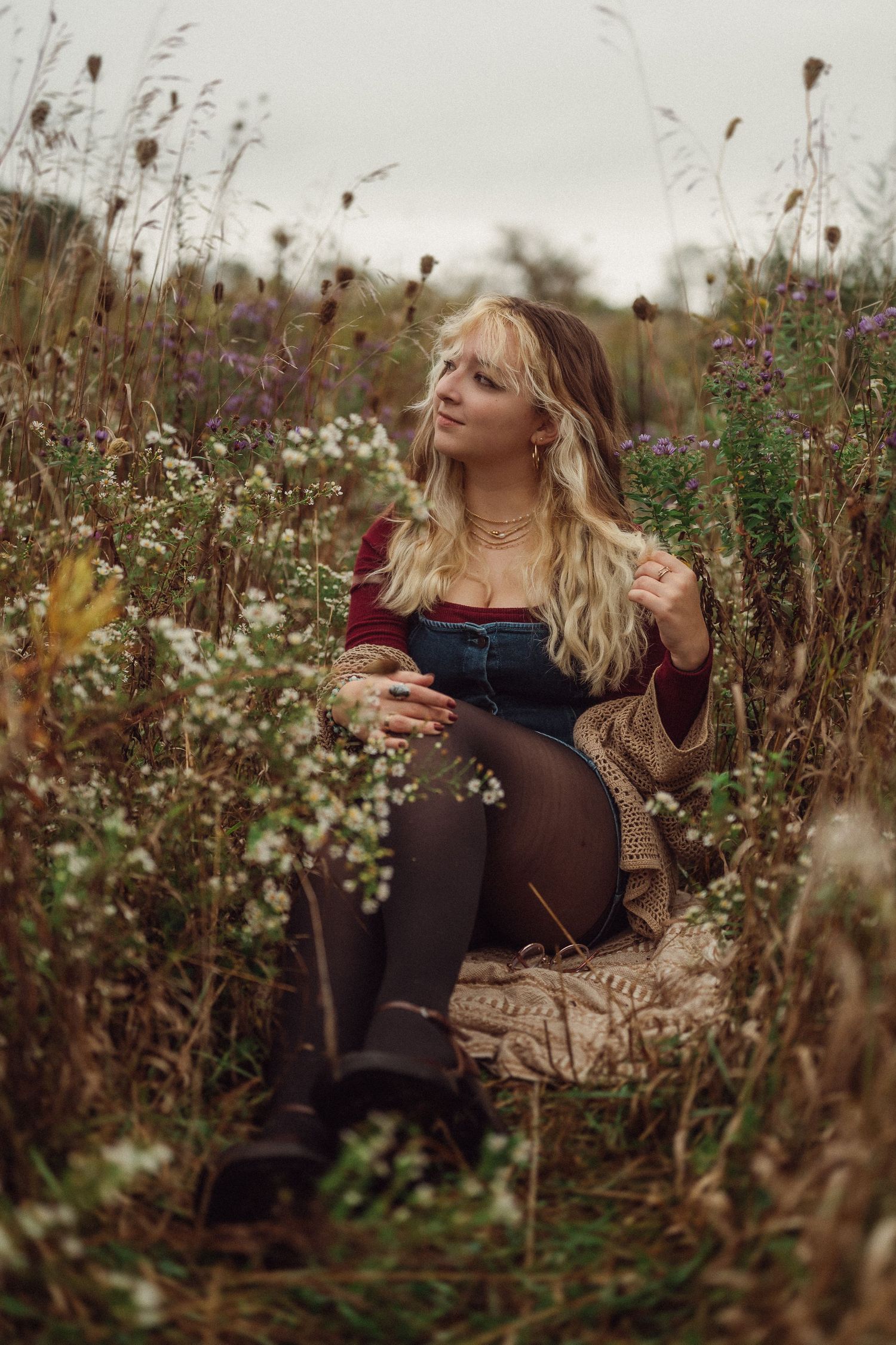 Cozy autumn portrait in overalls and sweater seated among wildflowers.