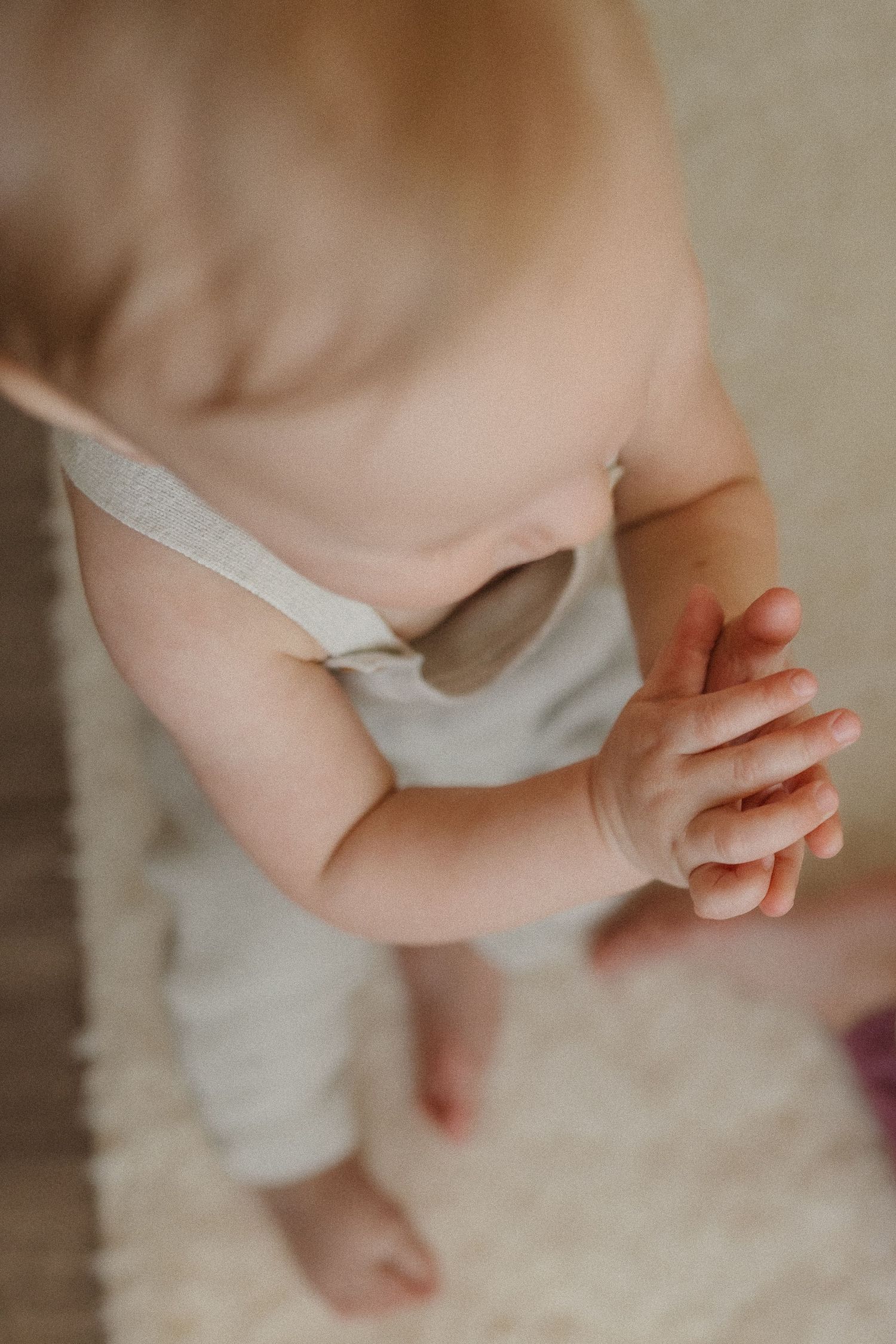 Close-up view of a baby wearing white overalls standing on plush carpet.