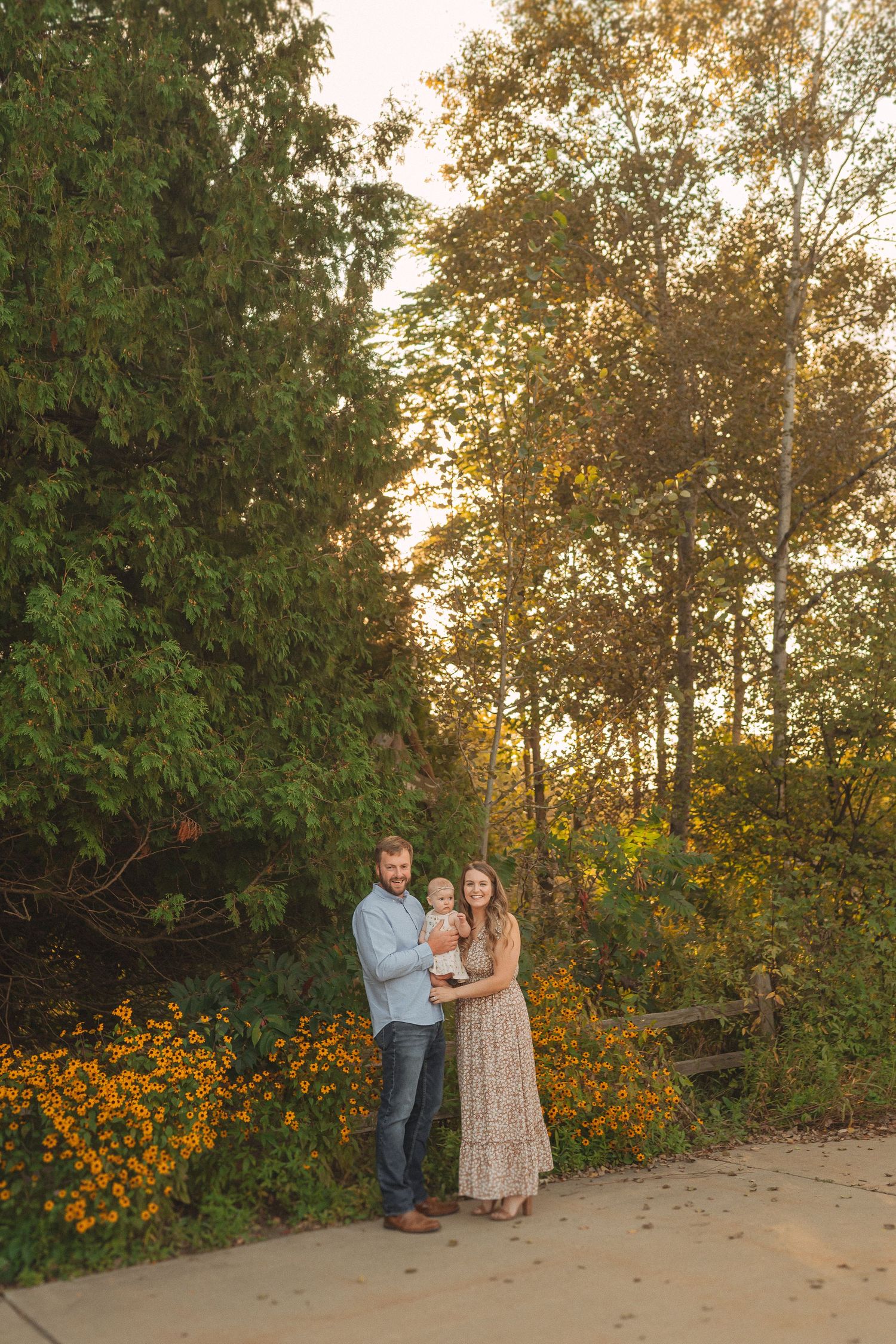 A family portrait in a garden setting with golden wildflowers and trees at sunset.