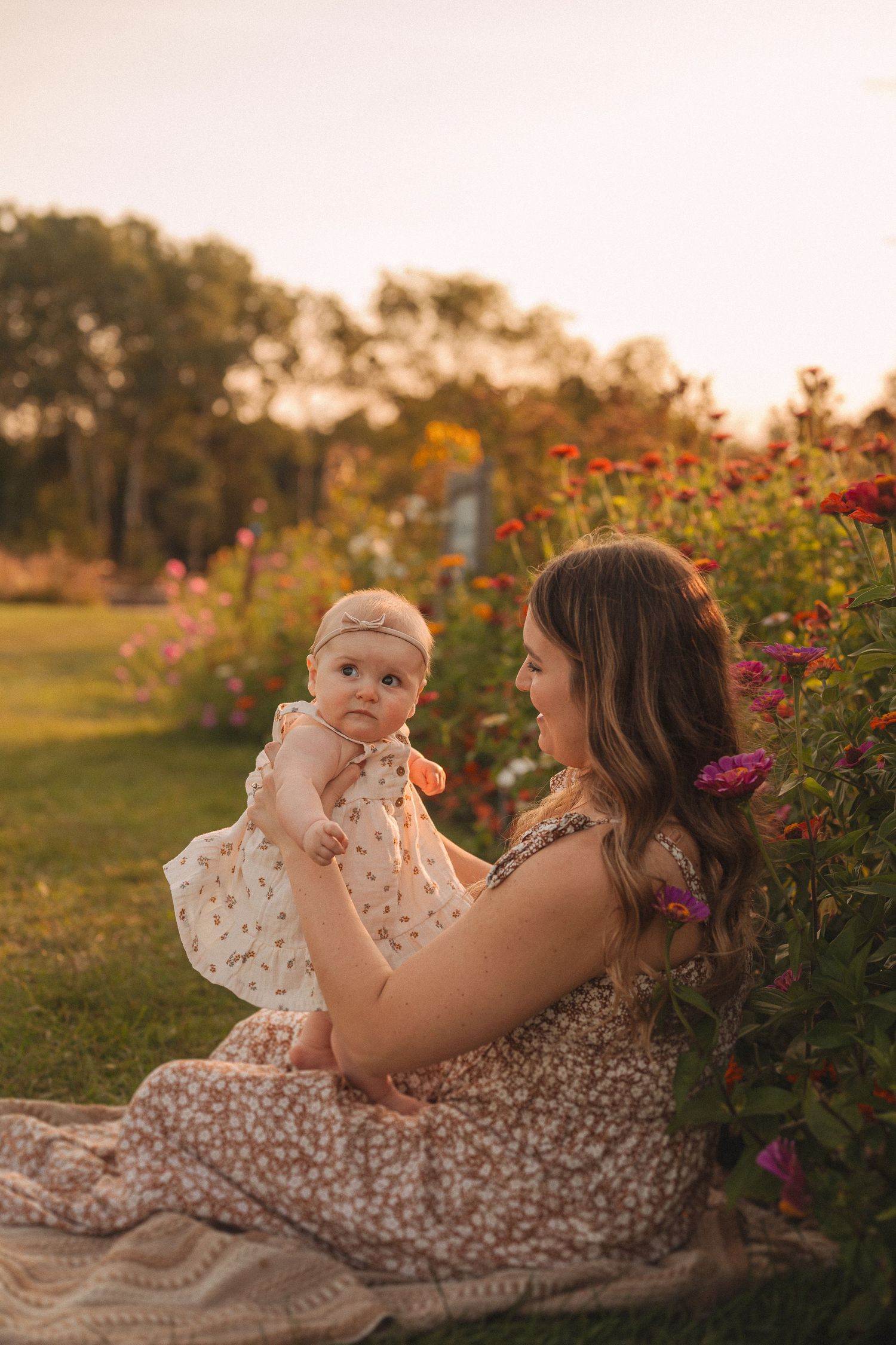 Warm sunset portrait in garden with floral dress seated among blooming flowers.
