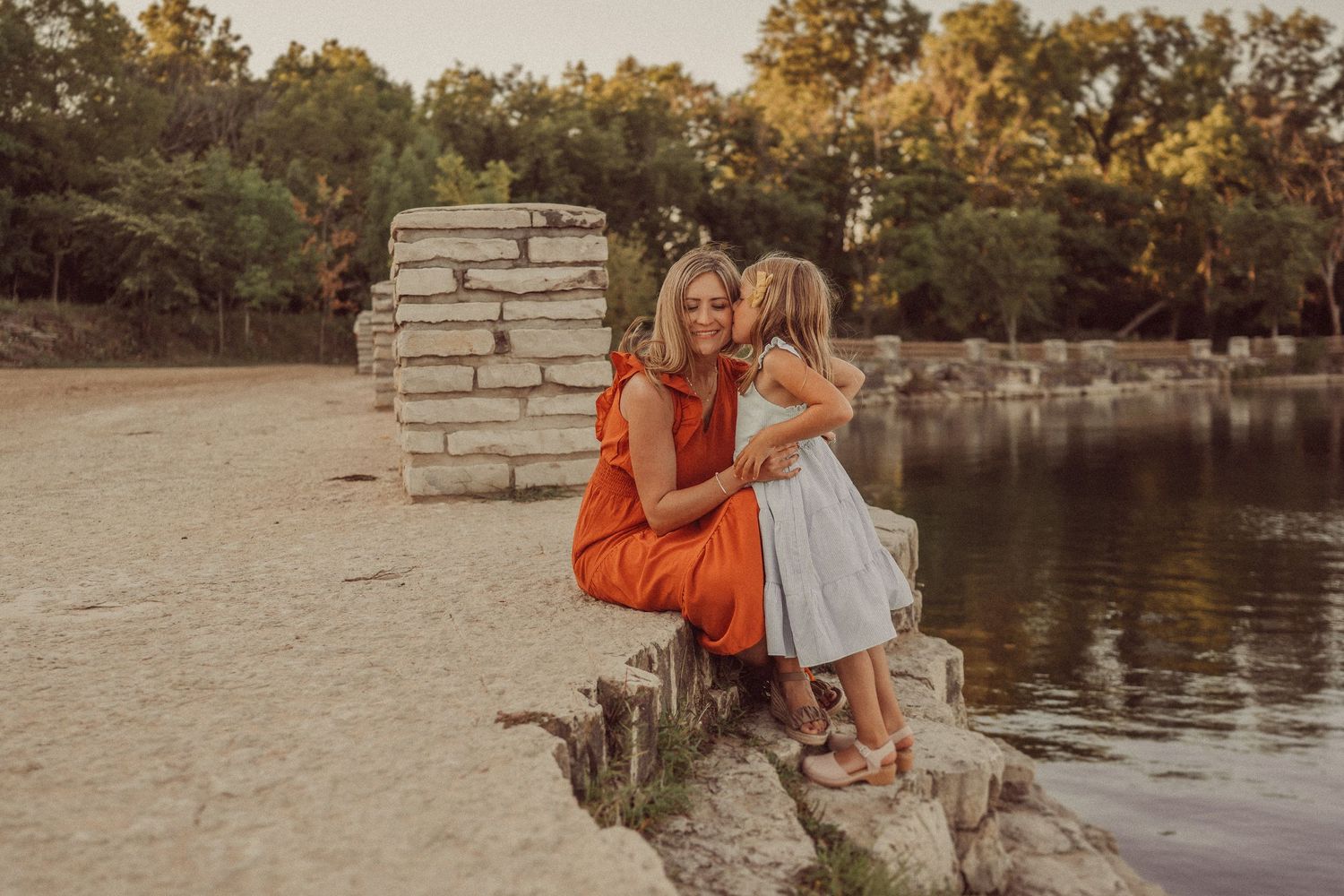 Sunset portrait by a lake showing intimate connection while sitting on stone blocks.