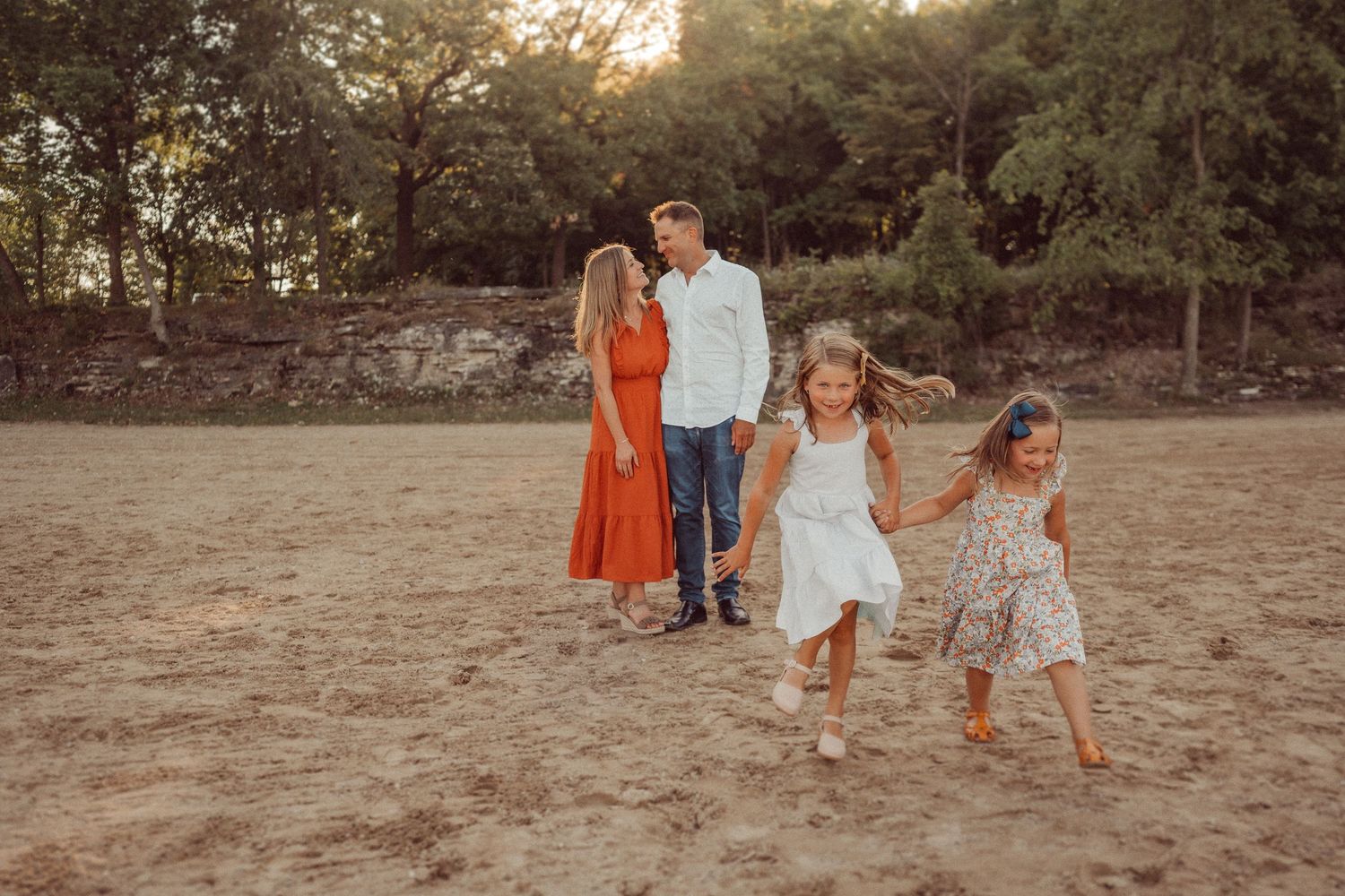A family in coordinated outfits poses together in a field at sunset.
