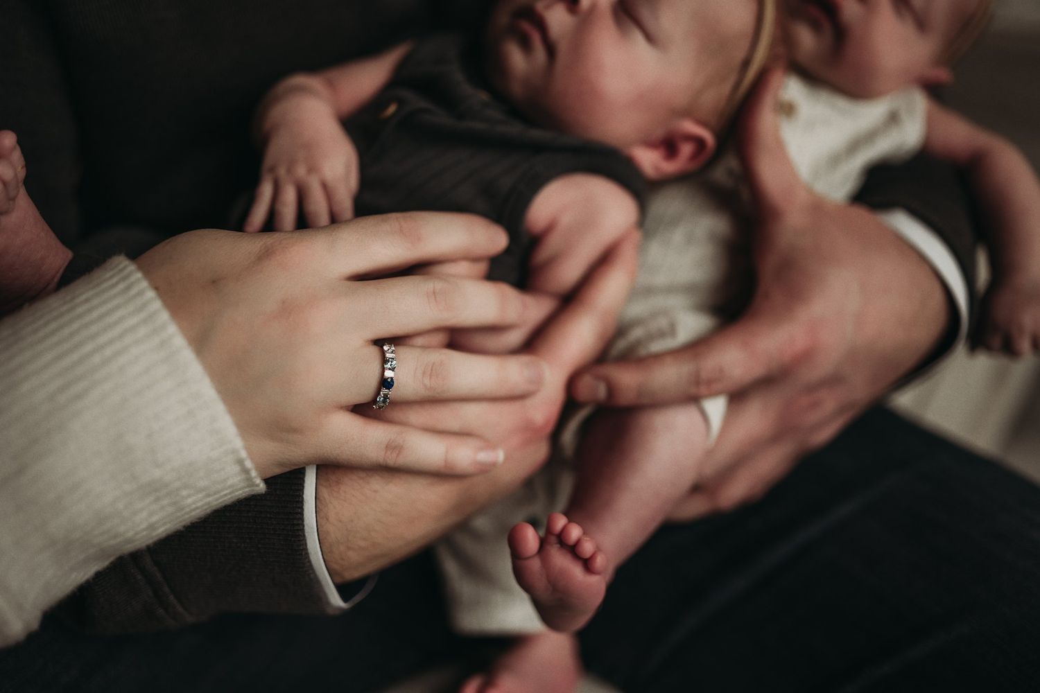 Close-up shot of hands holding a tiny infant's foot with wedding rings visible.