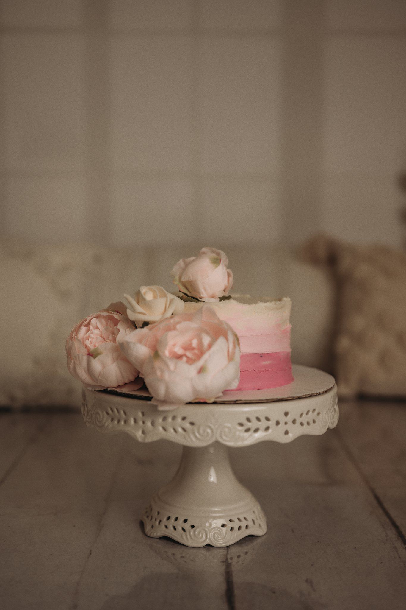 An elegant pink ombre cake with fresh roses on a white decorative cake stand.