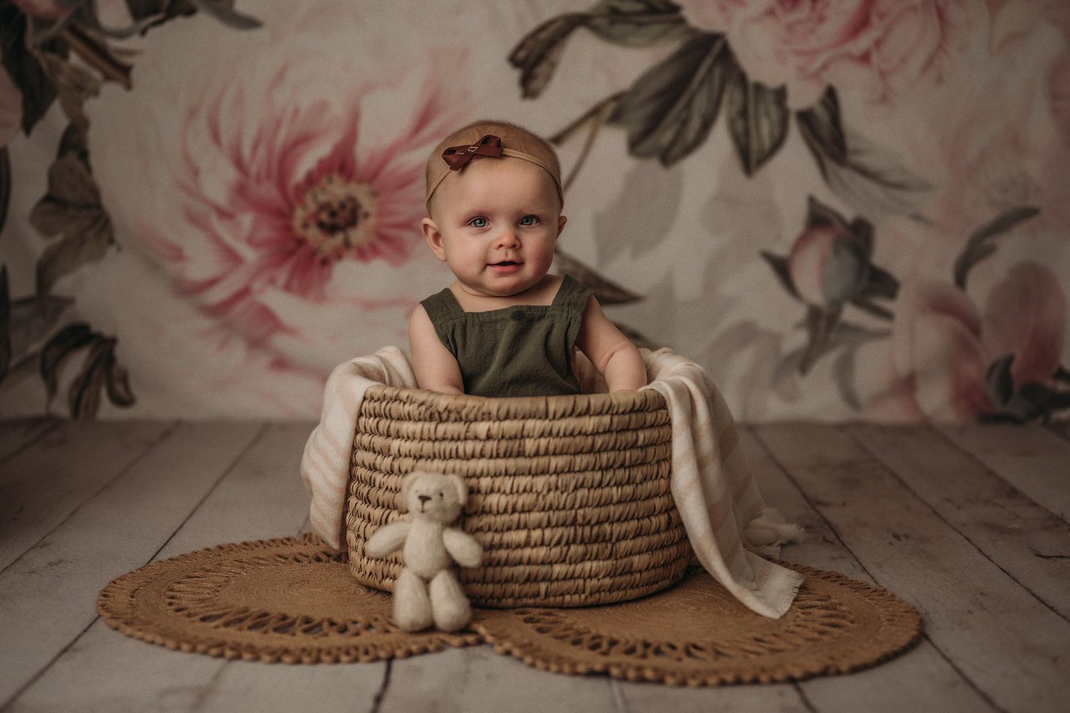 Studio portrait with child in basket against pink floral wallpaper.