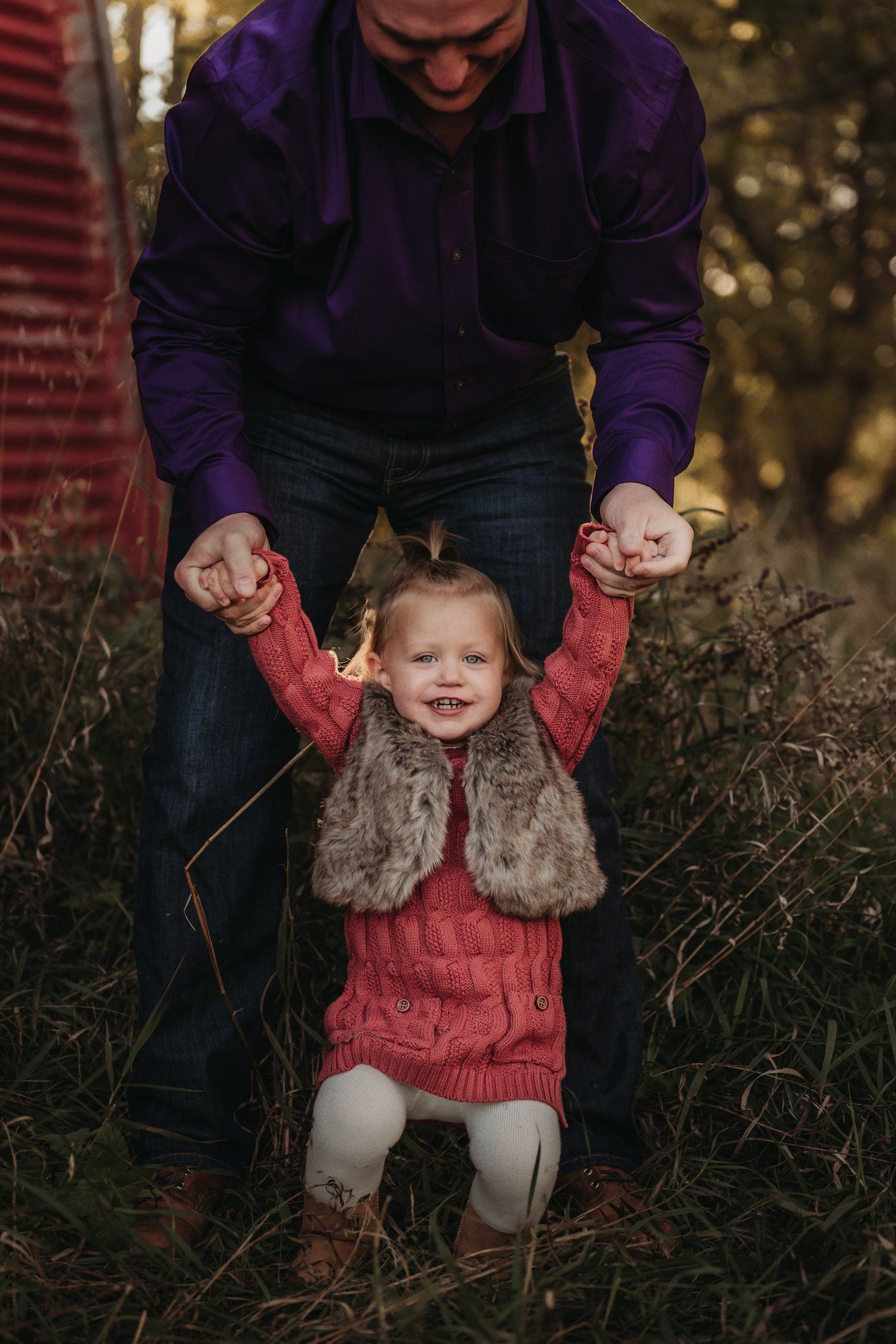 Child in fur vest and red dress holding hands with adult in purple jacket.