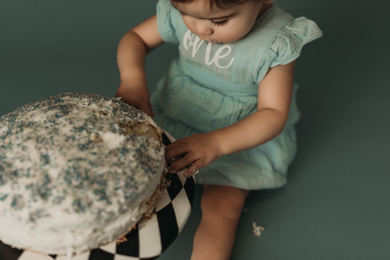 Close-up detail of a white frosted cake on a striped pedestal with scattered crumbs.